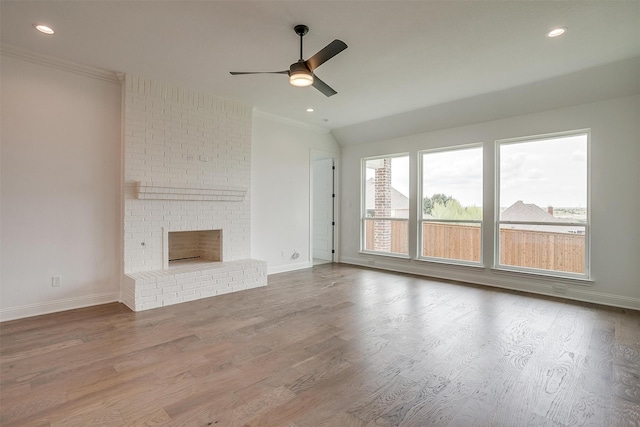 unfurnished living room with wood-type flooring, a brick fireplace, crown molding, and ceiling fan