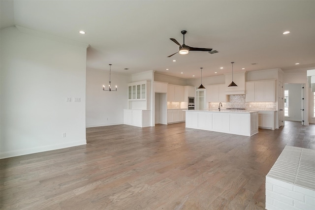 unfurnished living room featuring ceiling fan with notable chandelier, crown molding, sink, and light hardwood / wood-style flooring