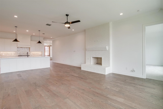 unfurnished living room featuring a brick fireplace, light wood-type flooring, crown molding, and ceiling fan