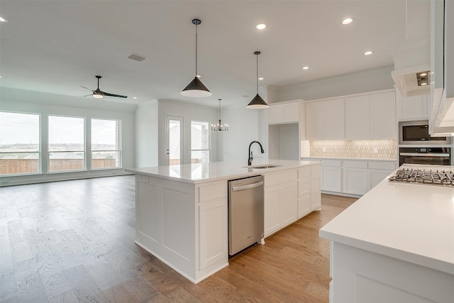 kitchen with an island with sink, stainless steel appliances, white cabinets, light hardwood / wood-style flooring, and backsplash