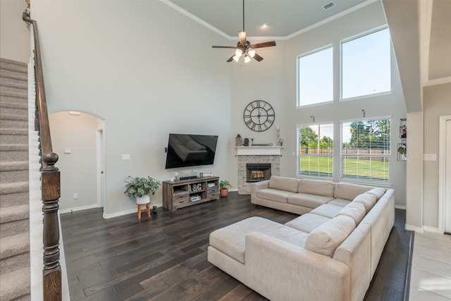 living room featuring a high ceiling, ceiling fan, dark hardwood / wood-style flooring, a stone fireplace, and ornamental molding