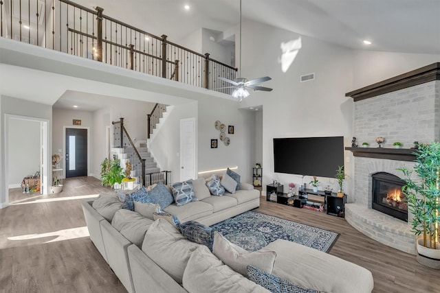 living room featuring ceiling fan, wood finished floors, visible vents, stairs, and a brick fireplace