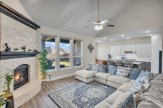 living area featuring a brick fireplace, baseboards, a ceiling fan, lofted ceiling, and light wood-style floors