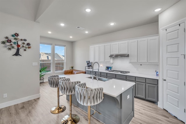 kitchen with a breakfast bar area, a sink, visible vents, light countertops, and a center island with sink