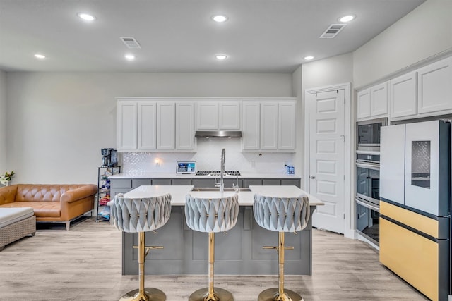 2104 Devonblue Dr, Forney, TX 75126 - kitchen with stainless steel appliances, under cabinet range hood, tasteful backsplash, light countertops, and a center island with sink