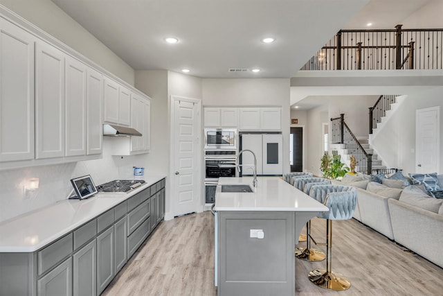 2104 Devonblue Dr, Forney, TX 75126 - kitchen featuring gray cabinetry, appliances with stainless steel finishes, under cabinet range hood, light wood-style floors, and open floor plan