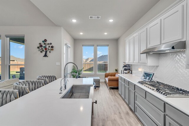 2104 Devonblue Dr, Forney, TX 75126 - kitchen featuring a sink, under cabinet range hood, stainless steel gas cooktop, open floor plan, and light wood-type flooring