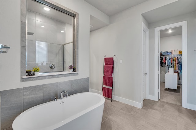 full bath with a soaking tub, a spacious closet, baseboards, and a tile shower