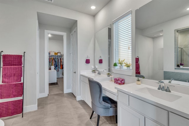 bathroom featuring a walk in closet, double vanity, recessed lighting, a sink, and baseboards