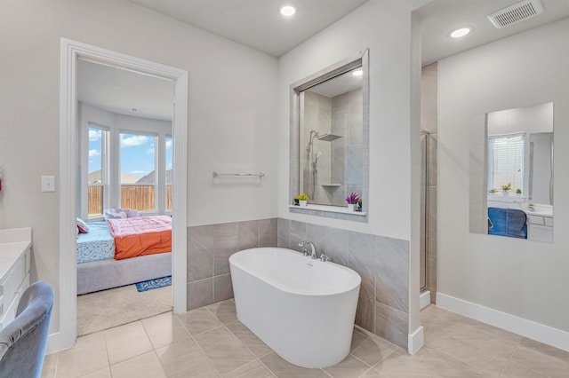 ensuite bathroom featuring visible vents, ensuite bathroom, tile patterned flooring, a freestanding bath, and tile walls