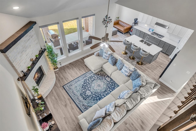 living area featuring recessed lighting, a brick fireplace, light wood-style flooring, and baseboards