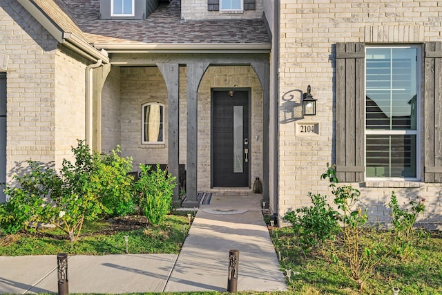 property entrance featuring a shingled roof and brick siding