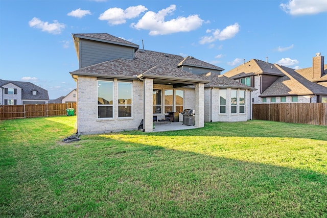 rear view of house featuring brick siding, a yard, a shingled roof, a patio area, and a fenced backyard