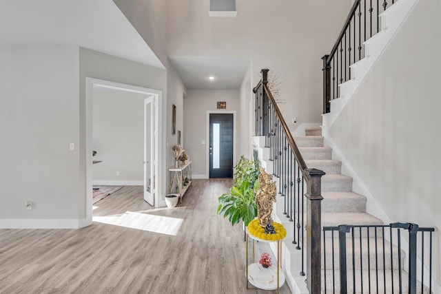 entryway with a towering ceiling, light wood finished floors, stairway, and baseboards