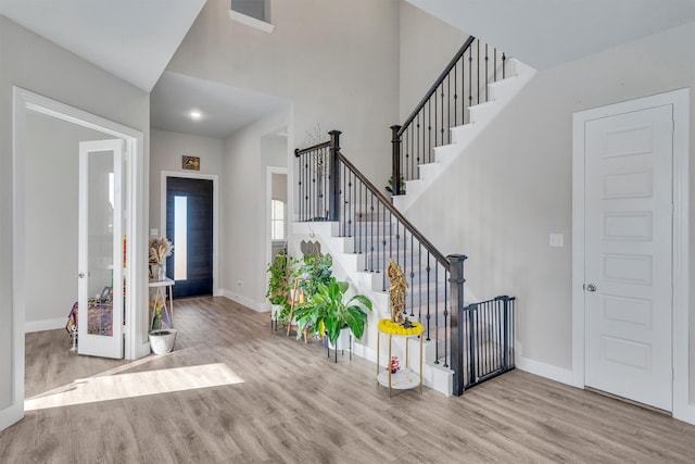 foyer featuring baseboards, a towering ceiling, light wood finished floors, and stairs