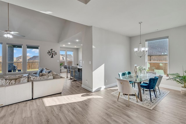 dining space featuring lofted ceiling, light wood-style flooring, baseboards, and ceiling fan with notable chandelier