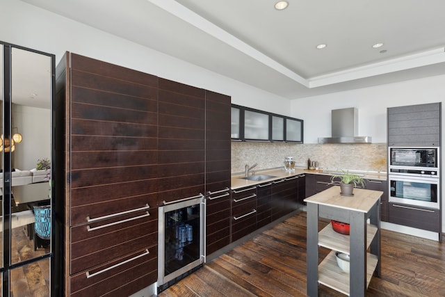 kitchen with dark wood-type flooring, oven, wall chimney exhaust hood, decorative backsplash, and beverage cooler