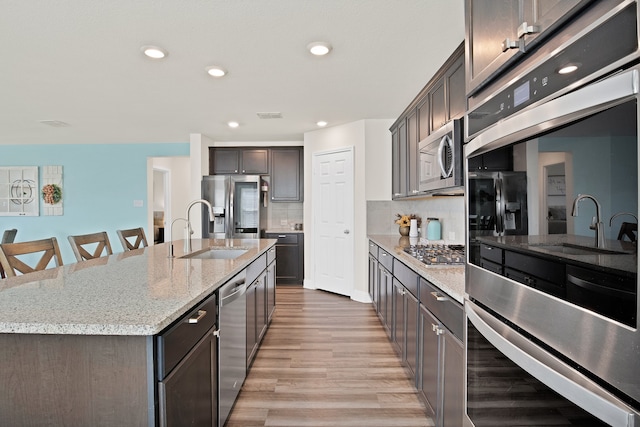 kitchen featuring sink, decorative backsplash, light wood-type flooring, an island with sink, and appliances with stainless steel finishes