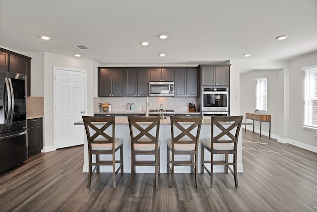 kitchen with dark hardwood / wood-style flooring, stainless steel appliances, tasteful backsplash, and a center island with sink