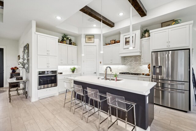 kitchen featuring beamed ceiling, sink, a kitchen island with sink, appliances with stainless steel finishes, and a breakfast bar