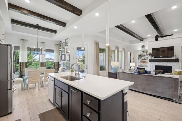 kitchen featuring sink, appliances with stainless steel finishes, beam ceiling, decorative light fixtures, and a center island with sink