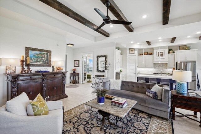 living room with light wood-type flooring, beamed ceiling, ceiling fan, and sink