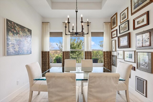 dining area featuring a raised ceiling, a notable chandelier, and light wood-type flooring