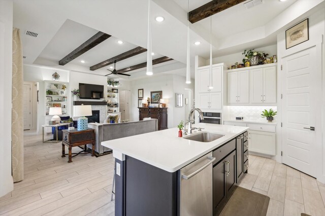 kitchen with beamed ceiling, a kitchen island with sink, sink, pendant lighting, and white cabinetry