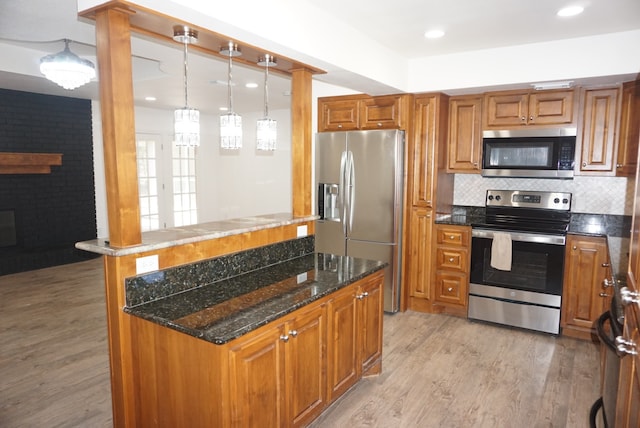 kitchen with dark stone counters, decorative light fixtures, appliances with stainless steel finishes, and light hardwood / wood-style flooring