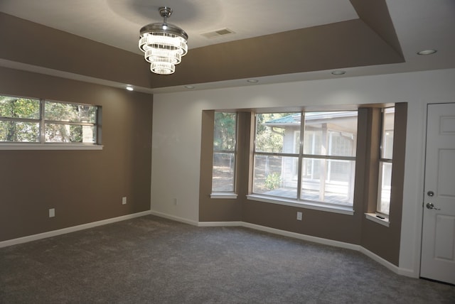 carpeted spare room featuring a tray ceiling and a notable chandelier