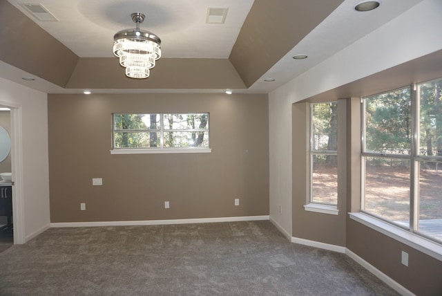 carpeted spare room with a tray ceiling, a chandelier, and a wealth of natural light