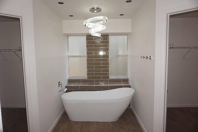 bathroom featuring an inviting chandelier, hardwood / wood-style flooring, backsplash, and a tub