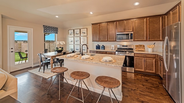 kitchen with stainless steel appliances, a center island with sink, sink, and dark wood-type flooring