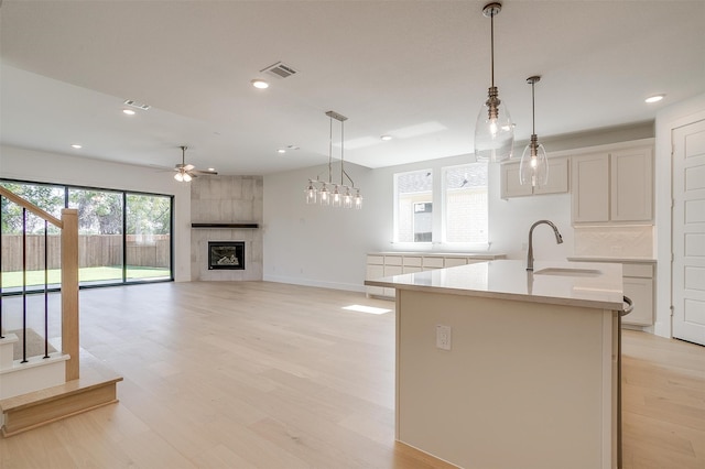 kitchen with an island with sink, light hardwood / wood-style flooring, hanging light fixtures, and a tile fireplace