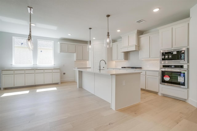 kitchen with light hardwood / wood-style floors, white cabinets, a center island with sink, and stainless steel gas stovetop