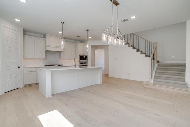 kitchen featuring pendant lighting, a kitchen island with sink, light hardwood / wood-style flooring, stainless steel appliances, and decorative backsplash