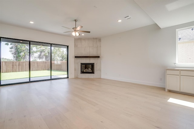 unfurnished living room with ceiling fan, a tile fireplace, and light hardwood / wood-style flooring