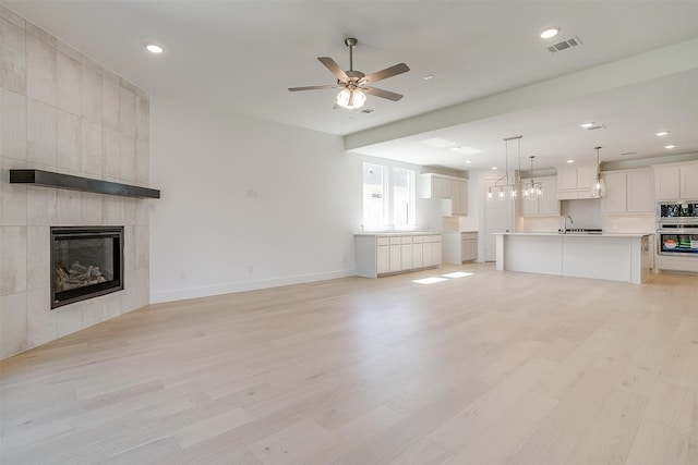 unfurnished living room with ceiling fan, a fireplace, and light hardwood / wood-style floors