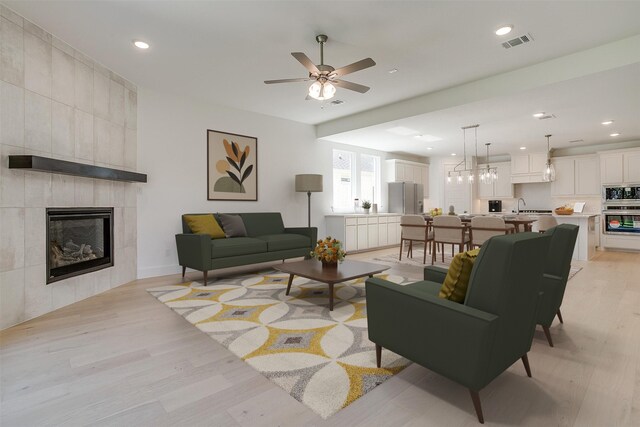 living room with light wood-type flooring, a fireplace, ceiling fan, and sink