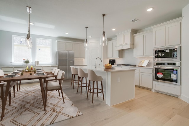 kitchen with a center island with sink, white cabinets, appliances with stainless steel finishes, and light hardwood / wood-style flooring