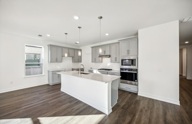 kitchen featuring decorative light fixtures, built in microwave, sink, oven, and a center island with sink