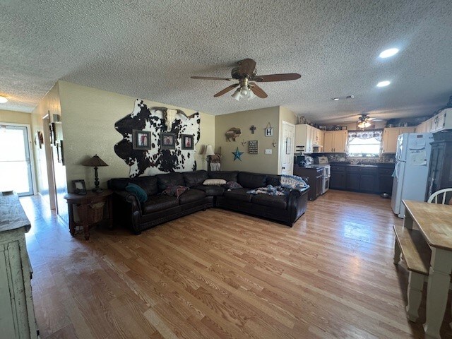 living room with ceiling fan, a textured ceiling, and light hardwood / wood-style flooring