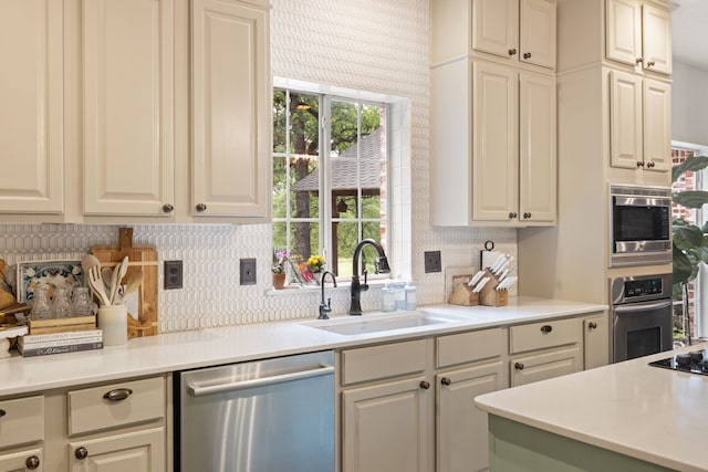 kitchen with backsplash, appliances with stainless steel finishes, sink, and cream cabinetry