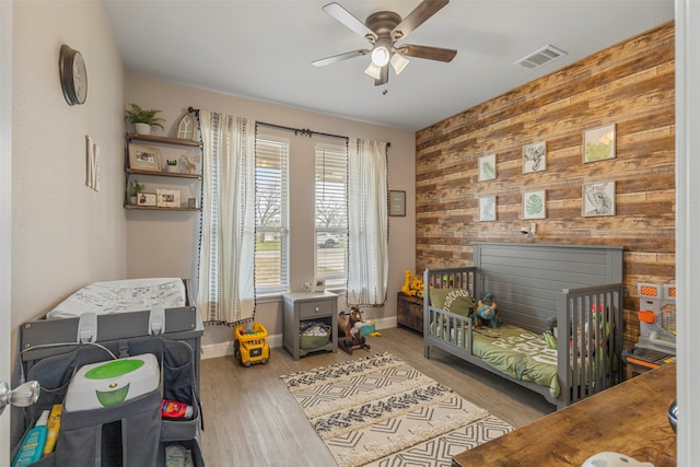 bedroom with ceiling fan, wood walls, and light hardwood / wood-style floors