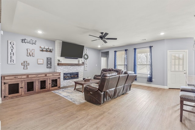 living room featuring ceiling fan, a stone fireplace, and light hardwood / wood-style flooring