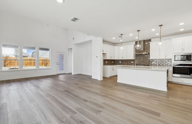 kitchen with stainless steel oven, pendant lighting, wall chimney range hood, a kitchen island with sink, and built in microwave