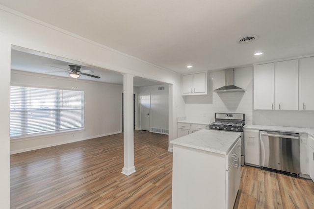 kitchen with a kitchen island, white cabinetry, stainless steel appliances, wall chimney range hood, and light hardwood / wood-style flooring