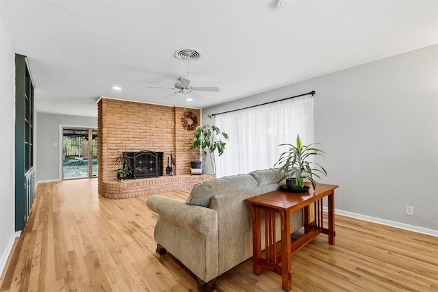 living room featuring light hardwood / wood-style flooring, a brick fireplace, and ceiling fan