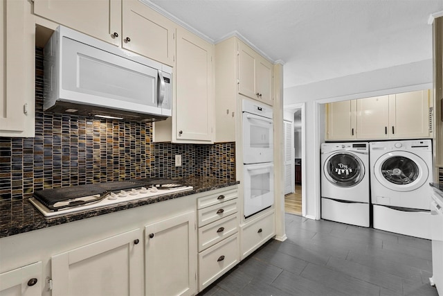 kitchen with white appliances, washing machine and clothes dryer, white cabinets, dark stone countertops, and decorative backsplash