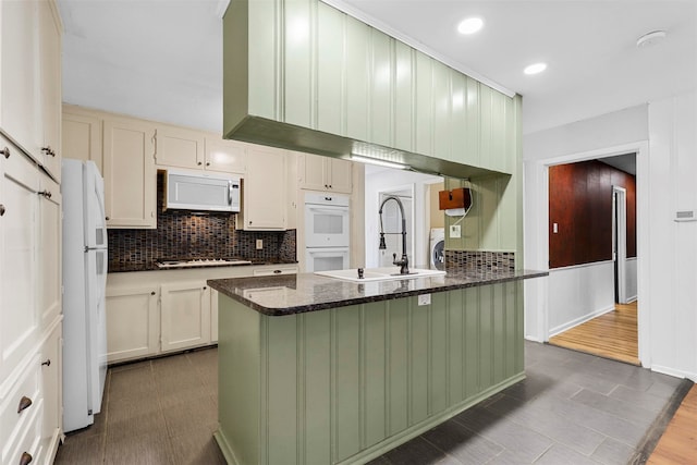 kitchen with white appliances, dark stone counters, sink, and hardwood / wood-style floors